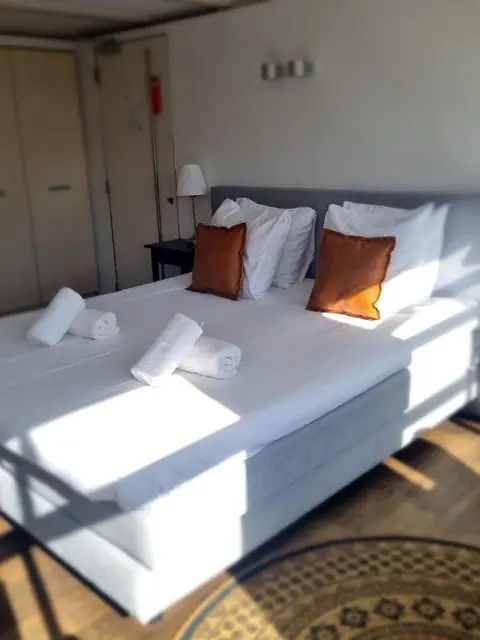 Kingsize kamer met wit opgemaakt bed en oranje kussens