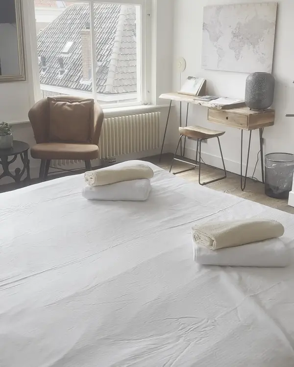 Lichte kamer met bed, fauteuil en bureau bij het raam